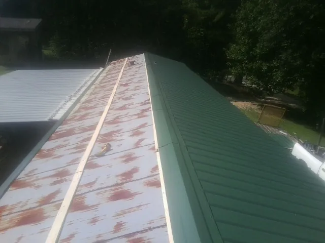 Old rusted panels beside newly installed green metal roofing — Wind Damage Roof Repair by Roofing Brothers in Highland